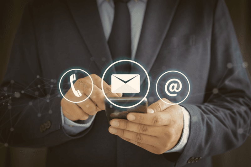 Phone, email and @ icons in front of a business person holding a smartphone