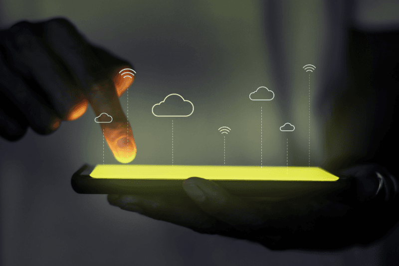 A hand touching cloud and wireless icons that rise from a glowing tablet screen